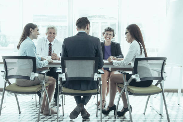 istock Cheerful business people in background looking at camera, while other colleagues talking at staff meeting. They sitting at table in board room. Business meeting concept 943042568