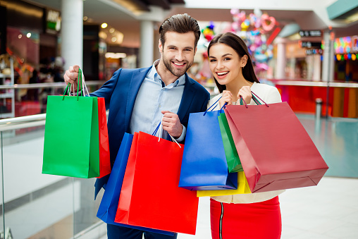 Portrait of happy lovely cute young woman with her handsome boyfriend  holding colored shopping packages and together walk  in modern mall.