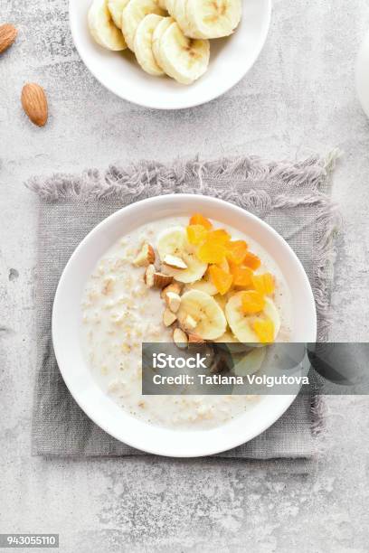 Oats Porridge With Banana Slices Nuts And Dried Apricot Stock Photo - Download Image Now