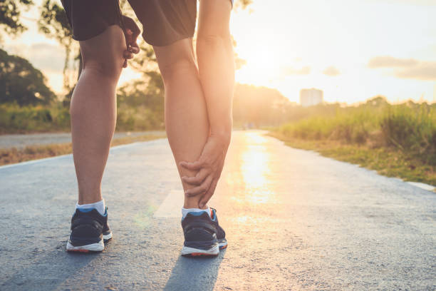 istock Injury from workout concept : Asian man use hands hold on his ankle while running on road in the park. Focus on ankle. 943058052