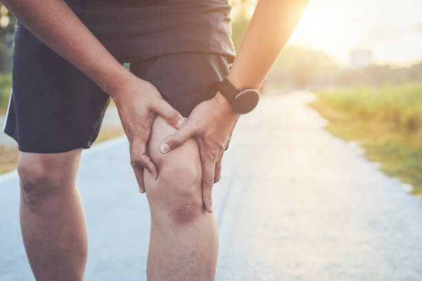 Injury from workout concept : The asian man use hands hold on his knee while running on road in the park. Shot in morning time, sunlight and warm effect with copy space for text or design lesiones por concepto de entrenamiento: hombre asiático uso manos sostienen sobre sus rodillas durante la ejecución de la carretera en el parque. disparo en efecto tiempo, luz solar y caliente de la mañana con espacio de copia de texto o diseño