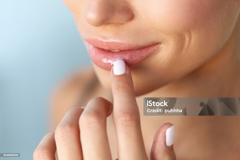 Lips Protection. Closeup of Healthy Woman Lips And Smooth Skin Lip Protection. Closeup of Beautiful Young Woman Healthy Lips. Female Model Smiling Mouth With Smooth Perfect Skin And Natural Manicure Touching Her Plush Lips. Lip Care And Beauty. High Resolution Human Lips Stock Photo