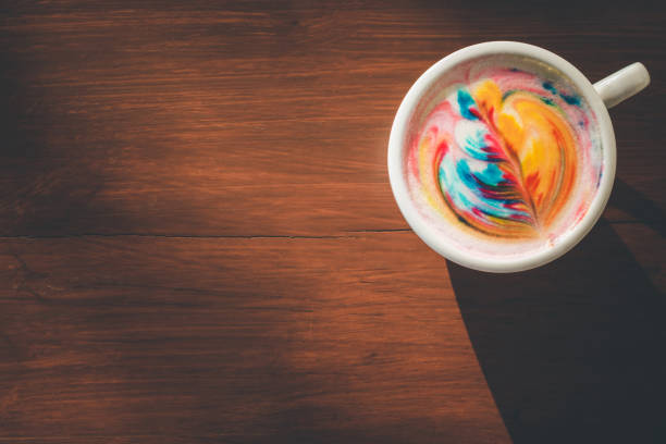 istock Colorful rainbow latte coffee in white cup on wooden table with copy space for text or design 943059342