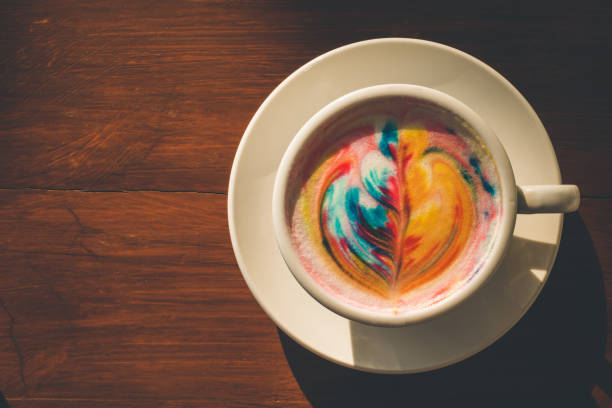 istock Colorful rainbow latte coffee in white cup on wooden table with copy space for text or design 943059402