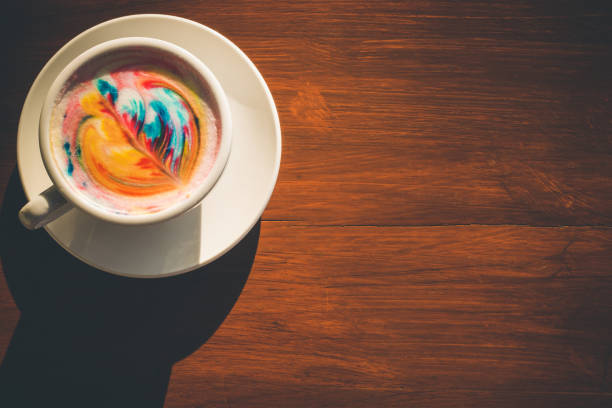 istock Colorful rainbow latte coffee in white cup on wooden table with copy space for text or design 943059434
