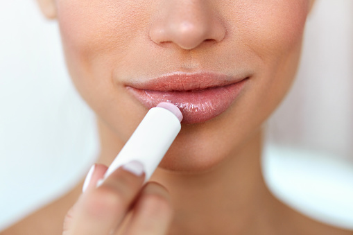 Lips Skin Care. Beautiful Woman Face With Full Lips Applying Hygienic Lip Balm, Lipcare Stick. Closeup Of Female Face With Soft Skin Putting Lip Protector Lipstick On. Beauty Cosmetics Concept