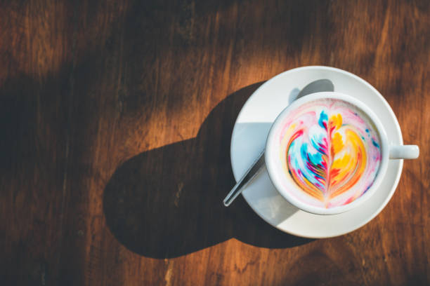 istock Colorful rainbow latte coffee in white cup on wooden table with copy space for text or design 943062982