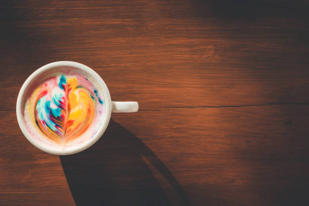 istock Colorful rainbow latte coffee in white cup on wooden table with copy space for text or design 943063096