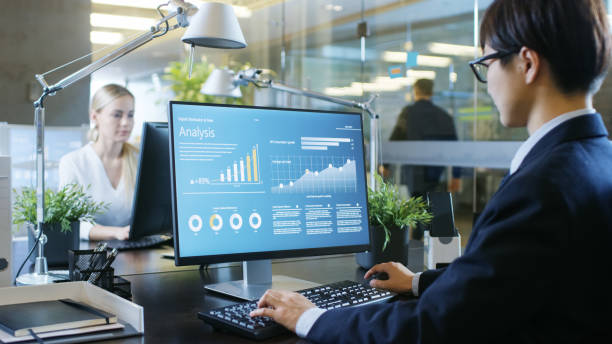 istock In the Office Businessman works at His Desk, He's Using Personal Computer with Statistical Information Showing on It's Screen. His Colleague Sets Opposite to Him. 943064550