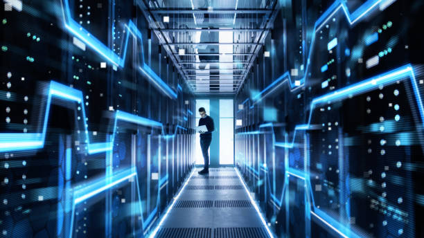 istock Male IT Engineer Works on a Laptop in a Big Data Center. Rows of Rack Servers with High Speed Internet Visualization. 943065400
