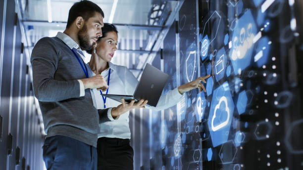 male it specialist holds laptop and discusses work with female server technician. they're standing in data center, rack server cabinet with cloud server icon and visualization. - cloud server imagens e fotografias de stock