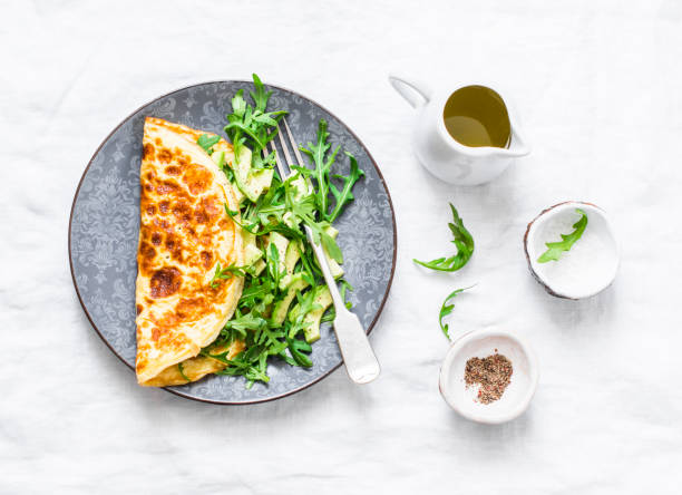 istock Omelette with cream cheese, arugula and avocado salad on a light background, top view.  Healthy breakfast or diet lunch 943074304