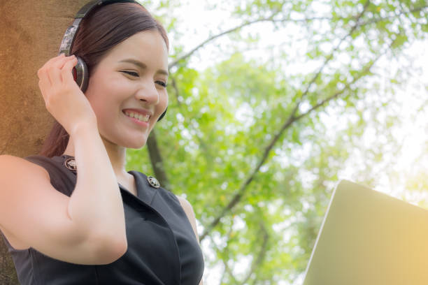 ビジネスの女性は、公園で音楽を聴くに頭電話を使用終了のハードワーク後彼女の仕事の後にリラックスして - office park audio ストックフォトと画像