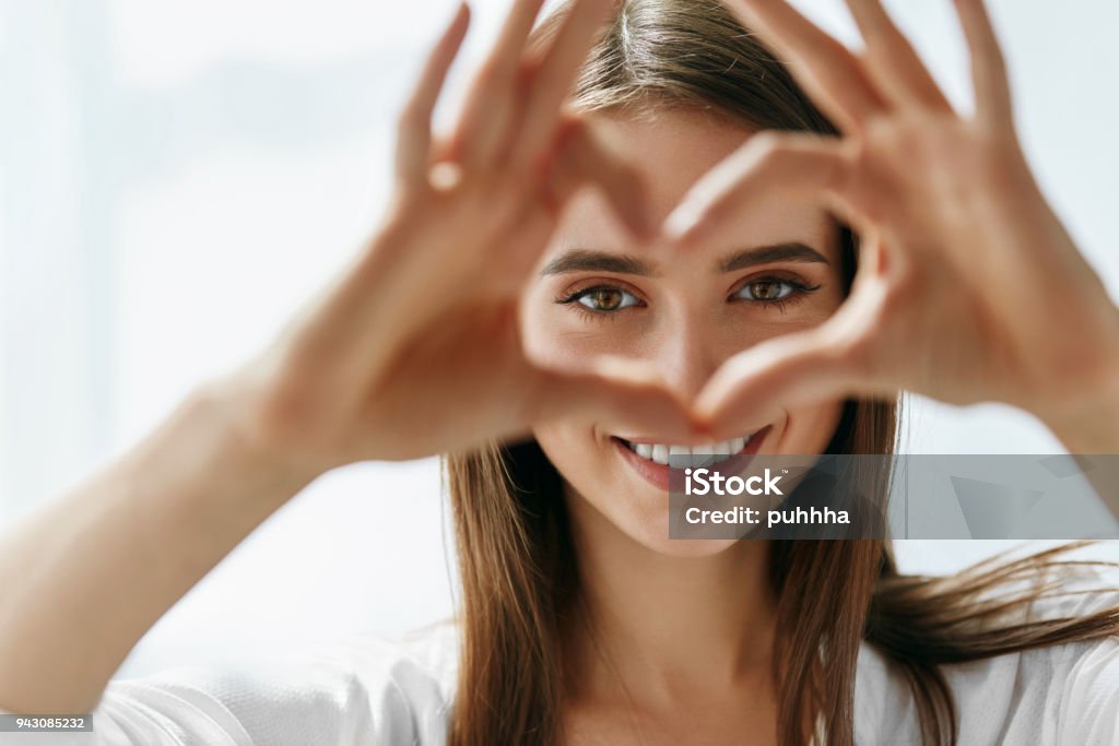 Beautiful Happy Woman Showing Love Sign Near Eyes. Healthy Eyes And Vision. Portrait Of Beautiful Happy Woman Holding Heart Shaped Hands Near Eyes. Closeup Of Smiling Girl With Healthy Skin Showing Love Sign. Eyecare. High Resolution Image Eye Stock Photo