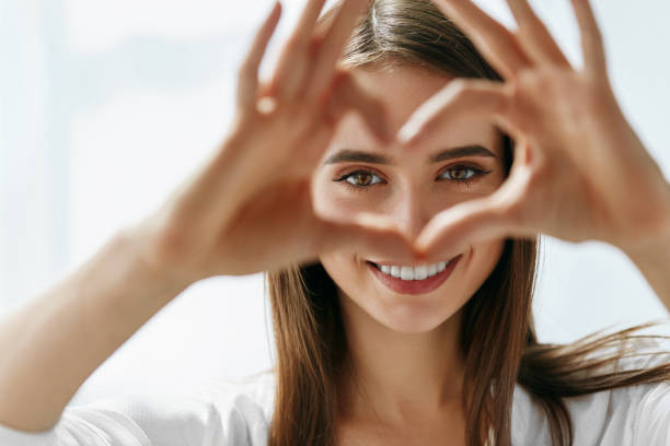 Beautiful Happy Woman Showing Love Sign Near Eyes. Healthy Eyes And Vision. Portrait Of Beautiful Happy Woman Holding Heart Shaped Hands Near Eyes. Closeup Of Smiling Girl With Healthy Skin Showing Love Sign. Eyecare. High Resolution Image forehead photos stock pictures, royalty-free photos & images