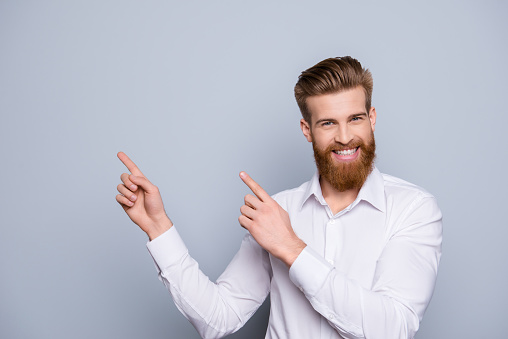 Portrait of serious confident bearded man pointing with fingers on copy space and smile