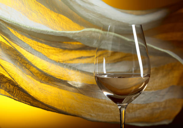 Glass of white wine on a yellow background. Yellow sheer fabric flutters in the wind. Copy space.