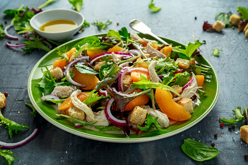 Fresh salad with chicken breast, peach, red onion, croutons and vegetables in a green plate. healthy food.