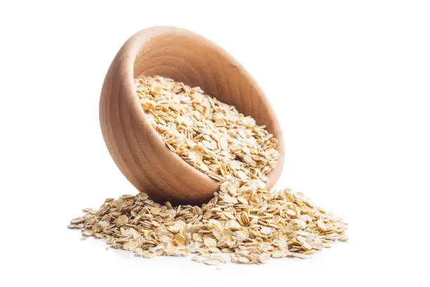 Dry rolled oatmeal in wooden bowl isolated on white background.