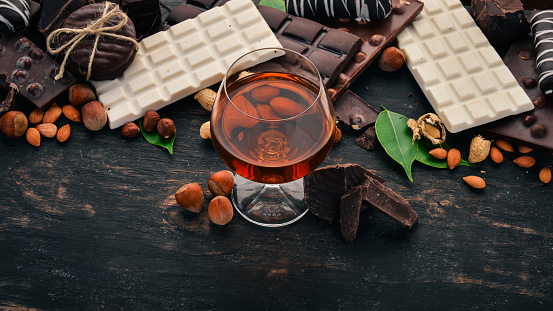 Una copa de coñac, brandy, whisky y un set de chocolate con galletas y dulces. Sobre un fondo negro de madera. Copiar el espacio para texto. photo