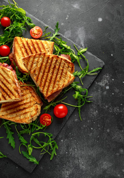 istock Grilled Bacon, cheese sandwich and served on stone platter with arugula and tomatoes 943107004