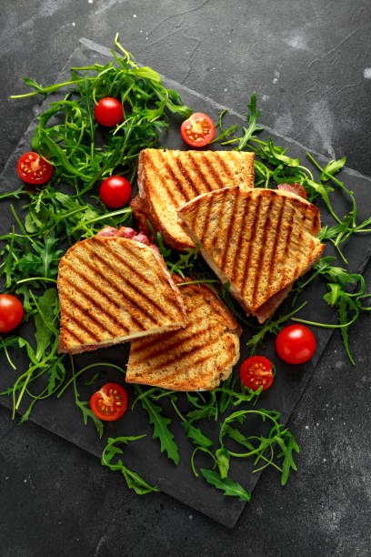 istock Grilled Bacon, cheese sandwich and served on stone platter with arugula and tomatoes 943107614