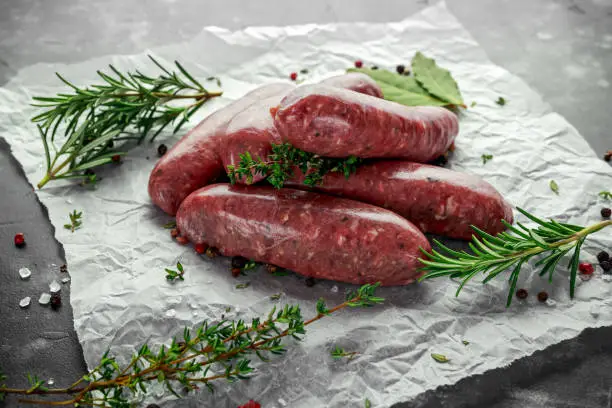 Photo of Freshly made raw breed butchers sausages in skins with herbs on crumpled paper