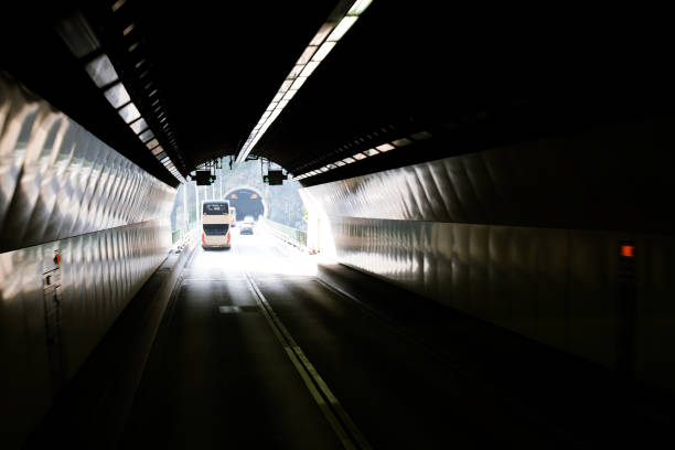 istock Urban Road With Marking Lines And Signs Passing Through Underground Tunnels Connected With Concrete Bridge. Public Transport And Vehicles On The Road. Sunlight At The End Of Tunnel. 943114798