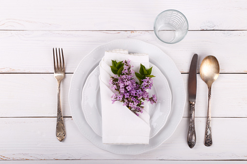 Spring festive table setting with vintage cutlery and lilac flowers on white wooden table,copy space flat lay