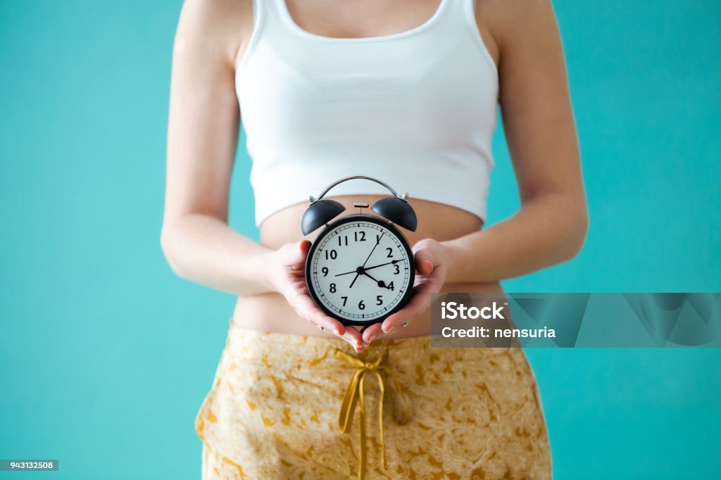 Giovane donna che tiene un orologio su sfondo blu. - Foto stock royalty-free di Orologio