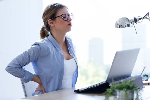 istock Tired young woman with back pain using her laptop at home. 943132636