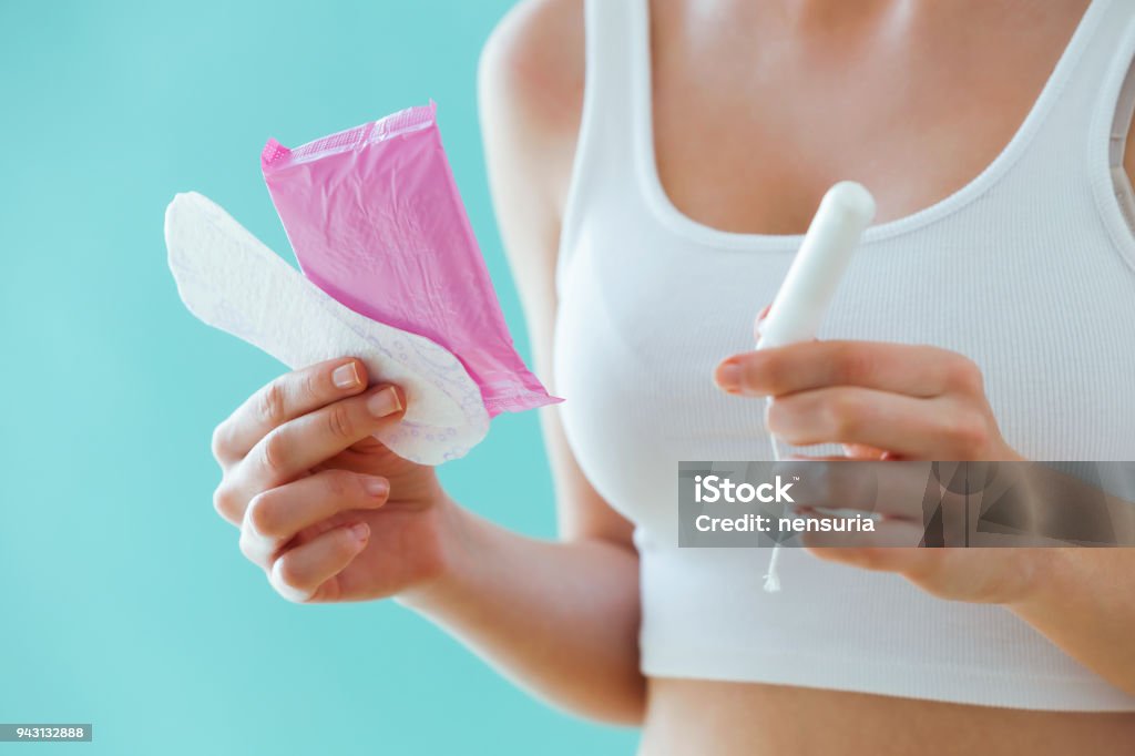 Young woman with a menstrual compress and a tampon on blue background. Close-up of young woman with a menstrual compress and a tampon on blue background. Menstruation Stock Photo