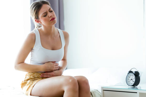 enfermiza mujer joven con dolor de estómago, apoyado en el sofá en casa. - belly ache fotografías e imágenes de stock