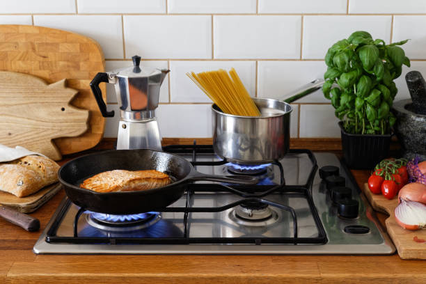 filet de saumon frit pan et spaghetti sur un gaz poêle dans cuisine maison traditionnelle. bois plan de travail. - gas counter photos et images de collection