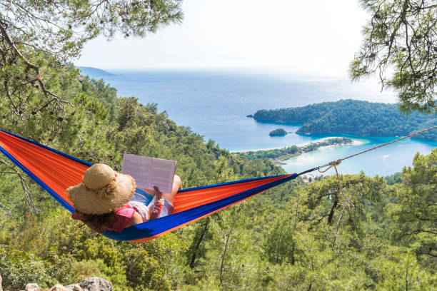 donna su un'amaca con libro in vacanza - summer vacations women hammock foto e immagini stock