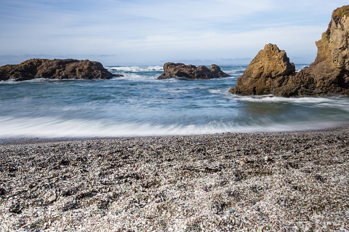 colorful glass pebbles blanket this beach in Fort Bragg, California. Photo taken with a slow shutter speed to show motion in the waves
