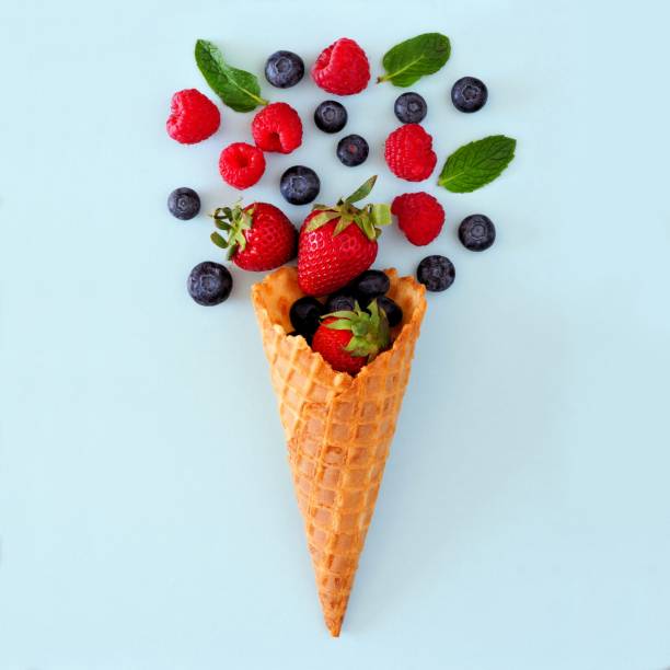 istock Mixed berries in ice cream cone. Flat lay over a blue background. 943188198