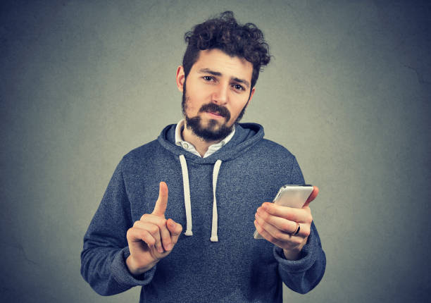 istock Man holding cell phone showing no, attention with finger hand gesture 943194878