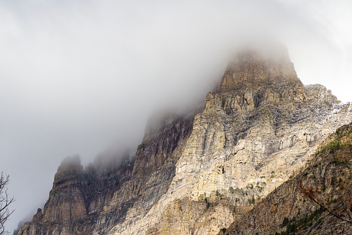 beautiful rocky mountains with colorful layers breaking thru the fog and clouds in Glacier National Park