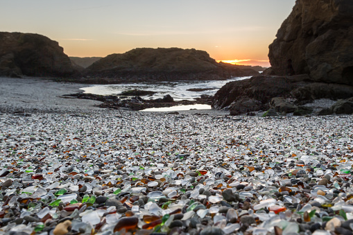 orange sun setting over the rocks lending a soft light to the colorful sea glass in this beach