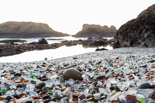 orange sun setting over the rocks lending a soft light to the colorful sea glass in this beach