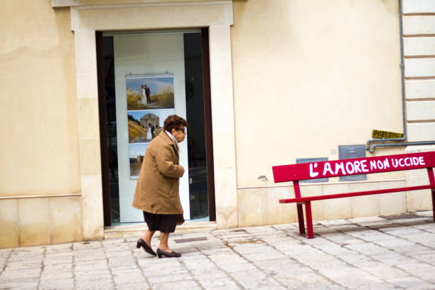 scicli, sicily: senior woman walking past red bench - scicli imagens e fotografias de stock