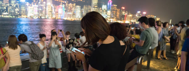 turyści gromadzą się wzdłuż walk of stars, aby zobaczyć i zrobić selfie z victoria harbor i handlowej panoramy w nocy. - refected zdjęcia i obrazy z banku zdjęć