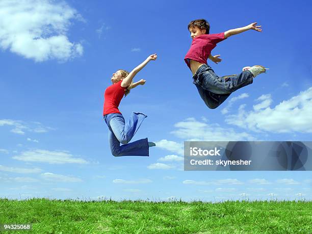 Girl And Child Jumping On Meadow Stock Photo - Download Image Now - Adult, Affectionate, Blue