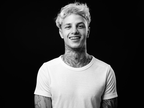 Studio Portrait Of Tattooed Young Man Against Black Background