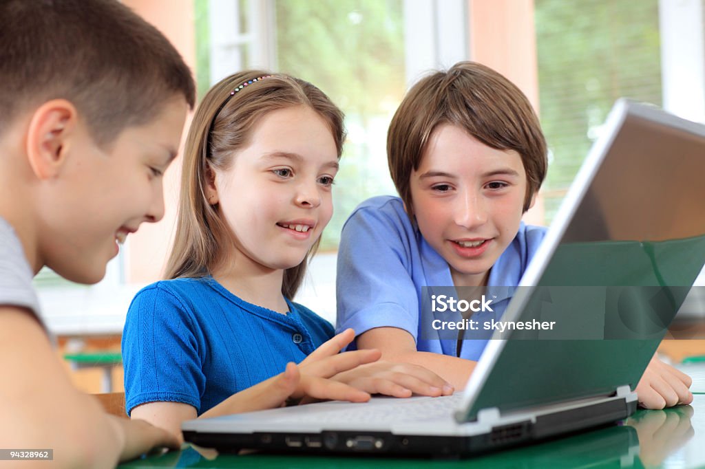 Schoolchildren having fun on laptops at classroom.  Blue Stock Photo