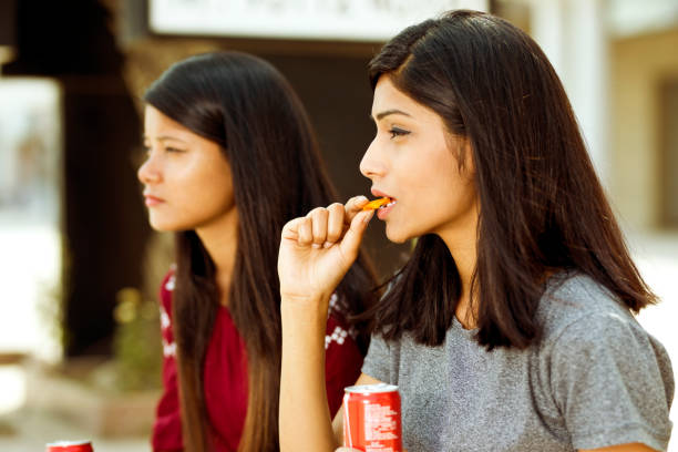 istock Young girls eating potato chips and holding drink can 943293480