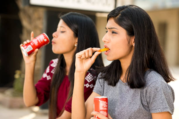 istock Young girls eating potato chips and holding drink can 943293490
