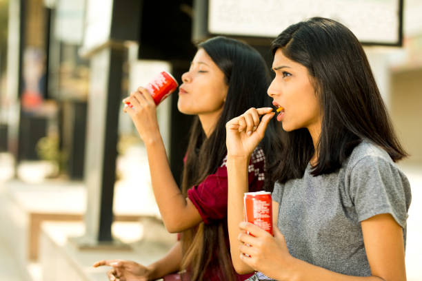istock Young girls eating potato chips and holding drink can 943293544