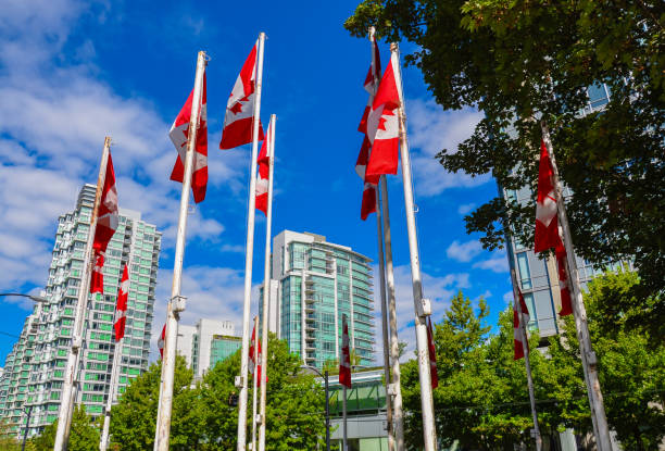 Flag of Canada. Canadian Flags in Vancouver BC. Flag poles with Canadian Flags with some buildings in the background shadow british columbia landscape cloudscape stock pictures, royalty-free photos & images